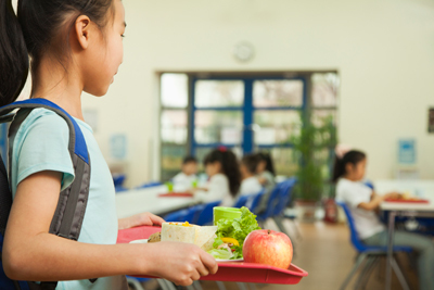 Elementary student with a tray of healthy food looks for a place to sit in the lunch room