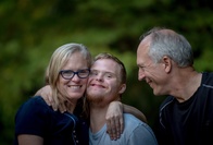 A young man with down syndrome is hugged by his father and mother 