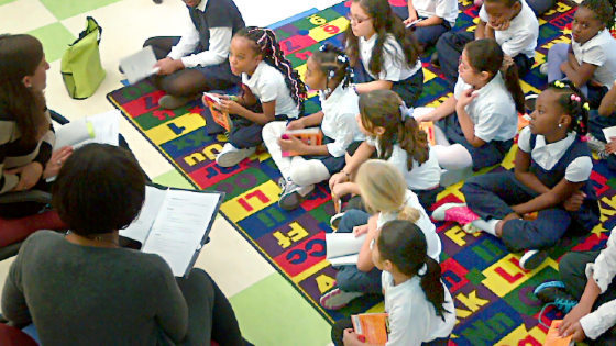 IMAGE: A group of children sit on a colorful rug with books in hand as they read along with Mayor Rawlings-Blake