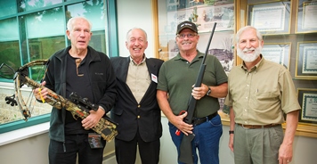 Two Michigan hunters hold a new crossbow and rifle with representatives from Safari Club International.
