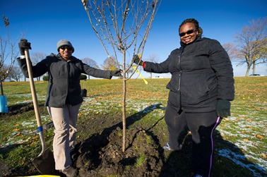 Two women holding a cherry tree to be planted on Belle Isle.