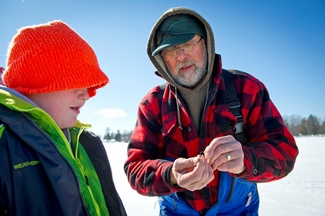 Volunteer instructor shows a young boy how to use a weight for ice fishing.