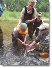 Fisheries biologist holding trout in river for students to see