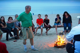 Campers sit by a fire on the beach.