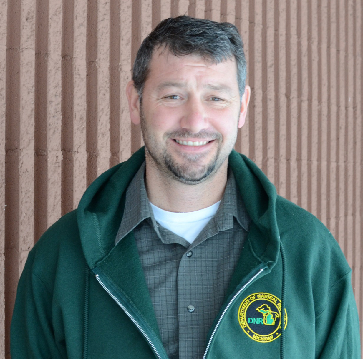 Kevin Swanson, DNR wildlife management specialist, dressed in a green DNR jacket outside the Marquette office.