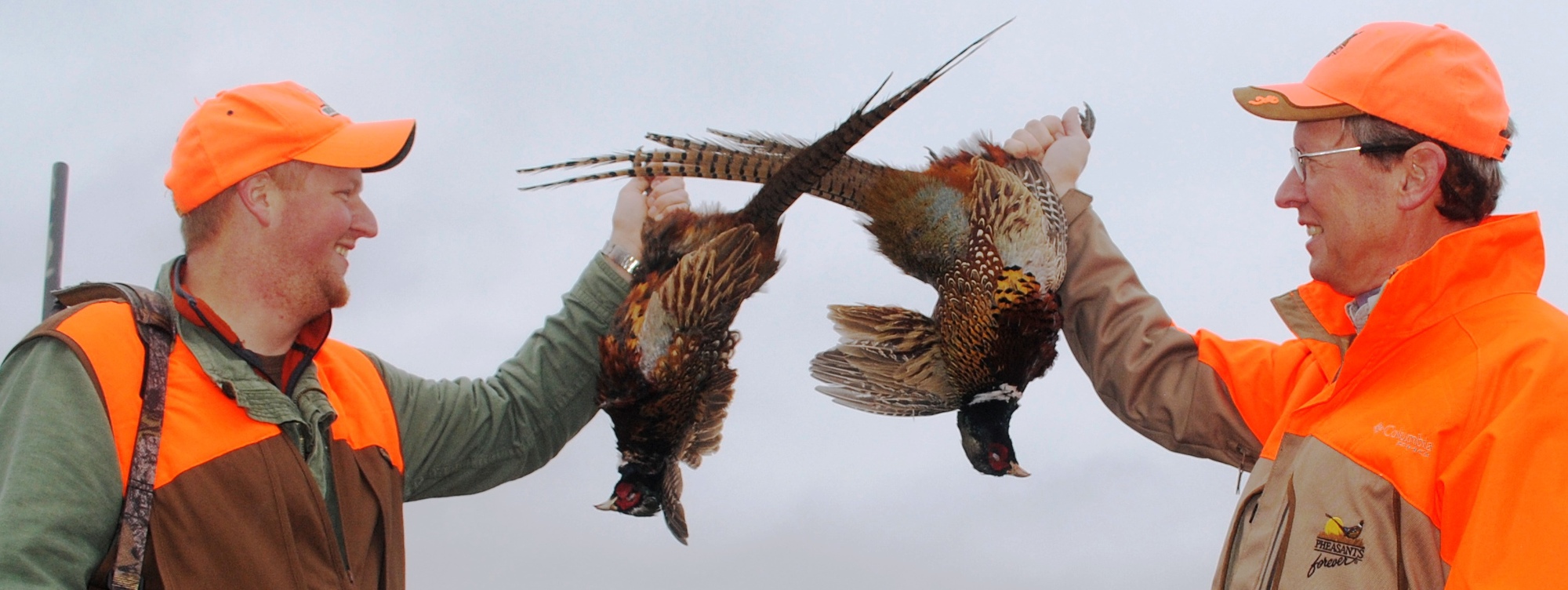 Two hunters dressed in hunter jackets hold one pheasant each they shot in Lower Michigan.