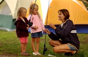 two young girls with fishing poles and their mom, tents in background