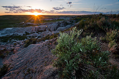 Sun sets over badlands with sagebrush.