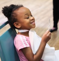 Young girl smiles into small mirror after receiving a dental checkup from OHCA Dentist Dr. Courtney Barrett. 