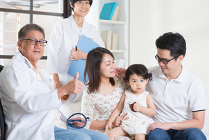 Pediatrician gives thumbs up beside happy family following a child's wellness exam