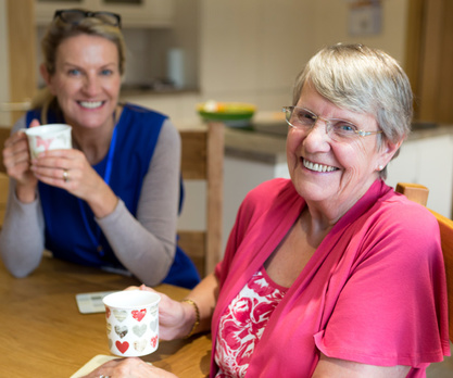 Image of an older woman in her home, smiling with an APS caseworker.