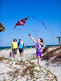 girl flying kite on beach, family nearby