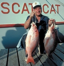 MAN HOLDING TWO LARGE RED SNAPPER BY BOAT NAMED "SCAT CAT"