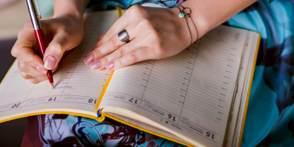 woman with bracelet writing with calendar on knee