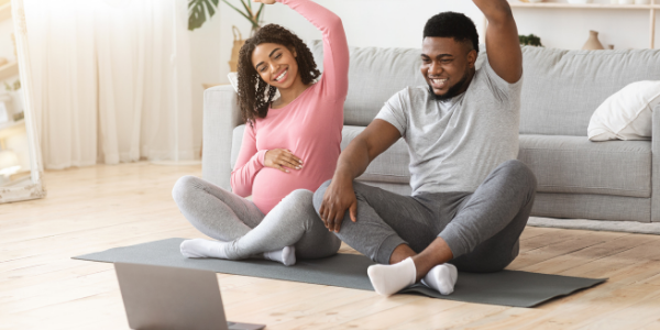 Pregnant lady and partner exercising in their living room to online exercise videos