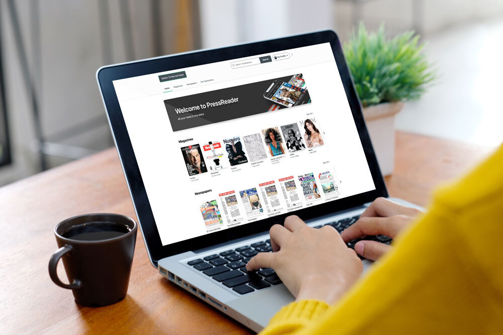 Promotional image for Pressreader accessibility. Featuring coffee, laptop and hands