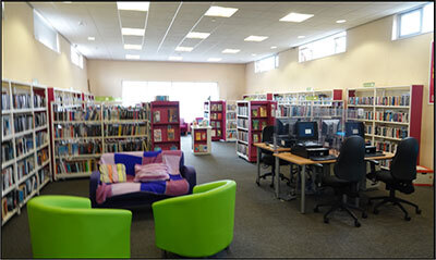 Image of interior of Birstall Library. Bright green chairs, bookshelves and desks with public computers.
