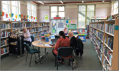 Heckmondwike Library showing bookshelves, people at table, children's area in background