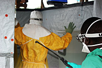 Clinician, assisted by a Médecins Sans Frontières staff member, following a protocol for decontamination before exiting an Ebola Treatment Unit.