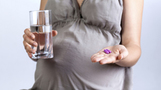 pregnant woman holding a glass of water and tablets