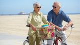 an elderly couple riding bikes on the beach