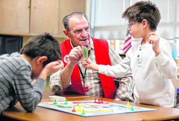 Foster Grandparent Donald Dauwen helps students at the South Dakota School for the Blind and Visually Impaired read a card as they play a board game.