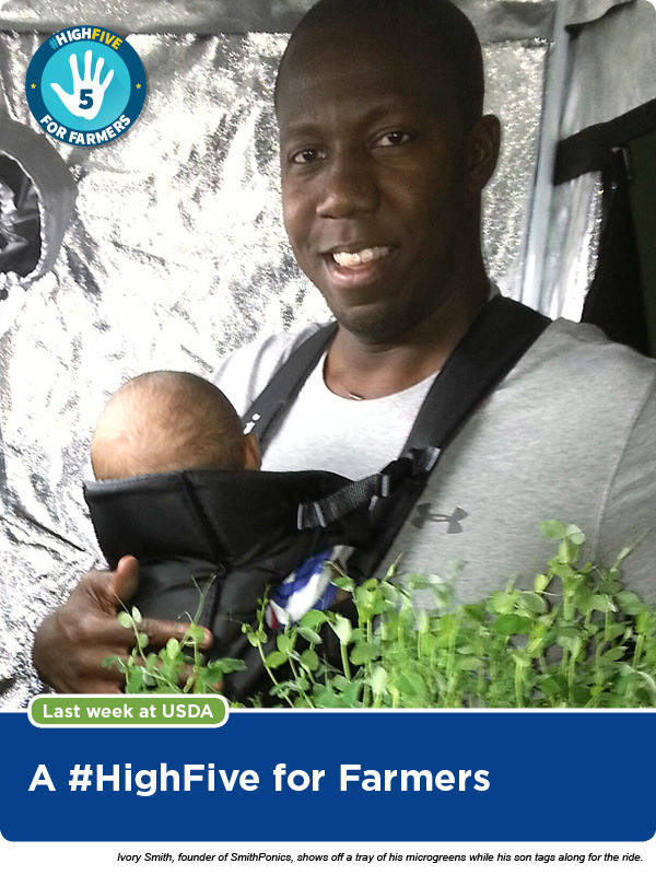 Ivory Smith, founder of SmithPonics, shows off a tray of his microgreens while his son tags along for the ride. 