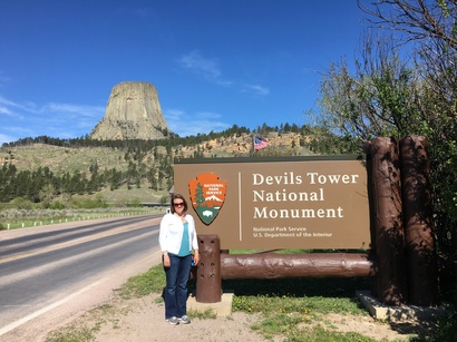 A woman, Heather Richardson, standing in front of the NPS sign for Devils Tower National Monument, with the rock formation in the background. 