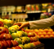 Image of a person reaching for apples in a grocery store.  