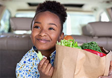 Girl in a car eats celery from a grocery bag.