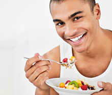 Man smiling and eating a bowl of fruit.