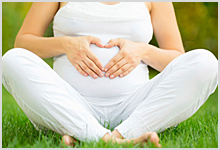 A pregnant woman sitting on grass.