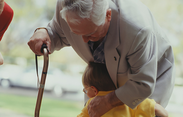 An elderly man with a cane being hugged by his grandson.