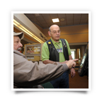 A Portland VAMC clerical staff member helps a Veteran use the VetLink kiosk. Pilot experiences indicate that circulating technology 'ambassadors' play an important role in technology acceptance and use. A Portland VAMC clerical staff member helps a Veteran use the VetLink kiosk. Pilot experiences indicate that circulating technology 'ambassadors' play an important role in technology acceptance and use.