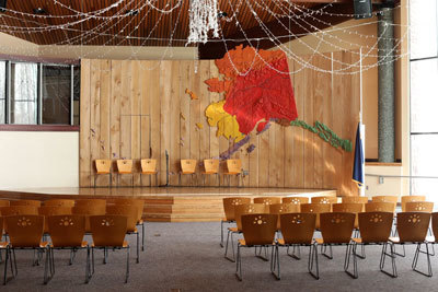 chairs face a small stage with Alaska map backdrop