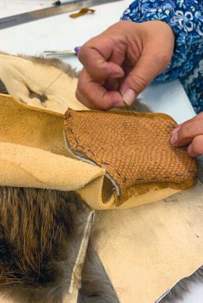 June Pardue sews a tanned salmon skin vamp onto bison hide with sea otter fur lying beneath