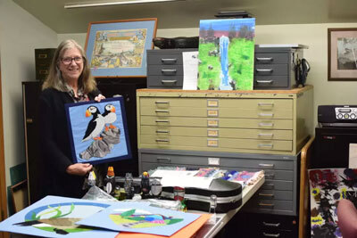 Cindi Lagoudakis pictured with stacks of community artwork before it was arranged for public view. 