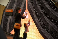 Two people stand with their hands on a lit up museum exhibit of a volcano.