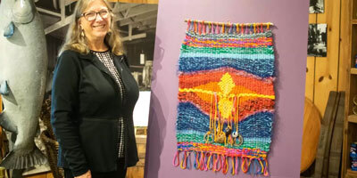 Cindi Lagoudakis stands next to a weaving by Suzanne Smith