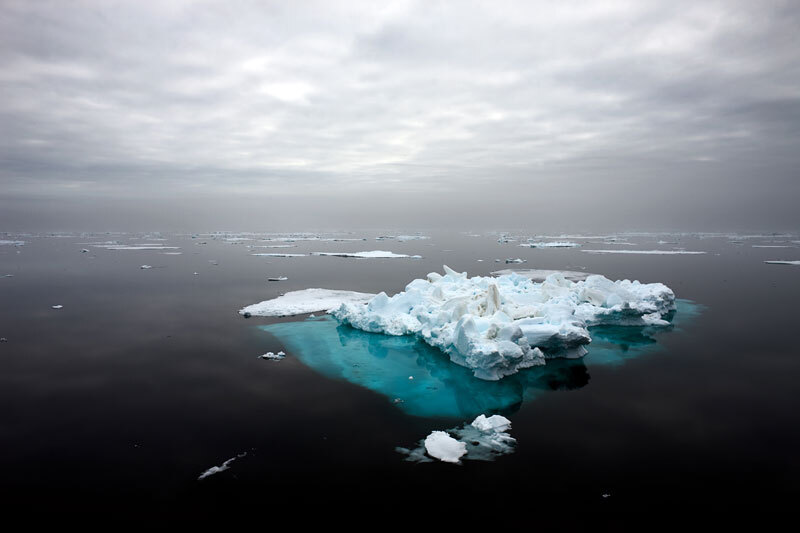 dark ocean, grey sky, vivid turquoise ice remnant in foreground