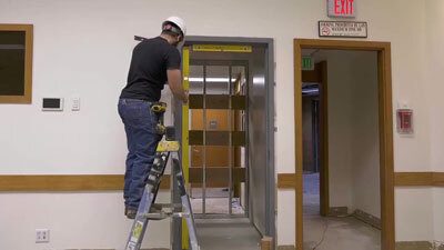 A worker uses a level in a doorway while balancing on a ladder