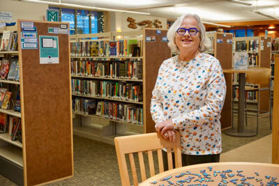 Cordova Public Library Director Geraldine de Rooy stands between the shelves of books in the library