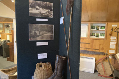 A display showcases boots, a creel basket, a fishing pole and net and various photos of summer history in Petersburg, Alaska.