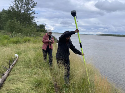 Tiffany Windholz and Maamcuk Foss walking along the bank of the Kuskokwim River, mapping the ongoing erosion in Akiak