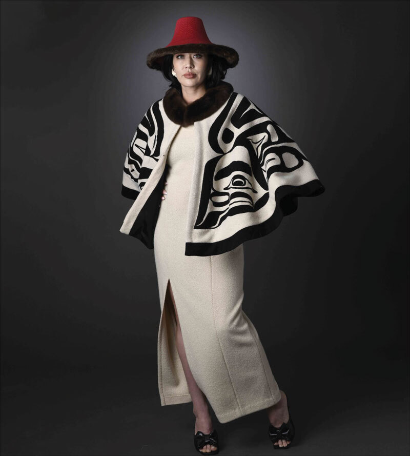 model wear cream and black formline cape with cream dress and red hat