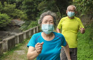 Senior couple jog through a park wearing masks.
