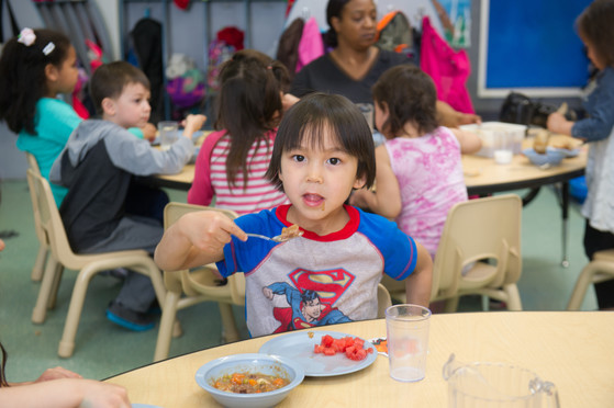 A child lifts a spoonful of delicious reindeer stew up to their mouth while the class eats lunch together.