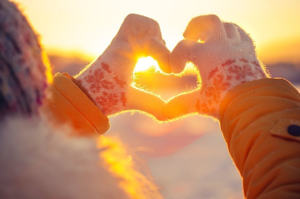 Two hands form a heart shape with a winter sunrise in the background.