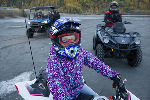 8 year old girl dressed for winter in Alaska wearing a helmet and sitting on an ATV is getting ready to go for a ride.