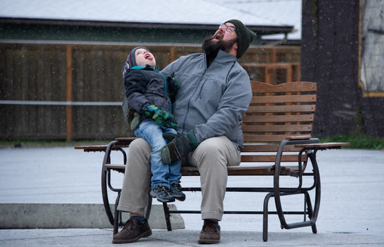 A man sits on a park bench with his son on his lap on a snowy day.
